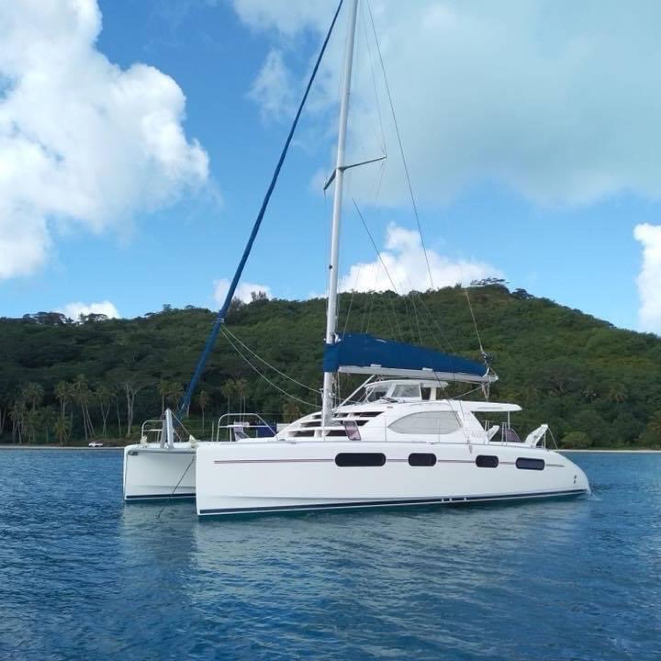 A white catamaran at anchor below green hills