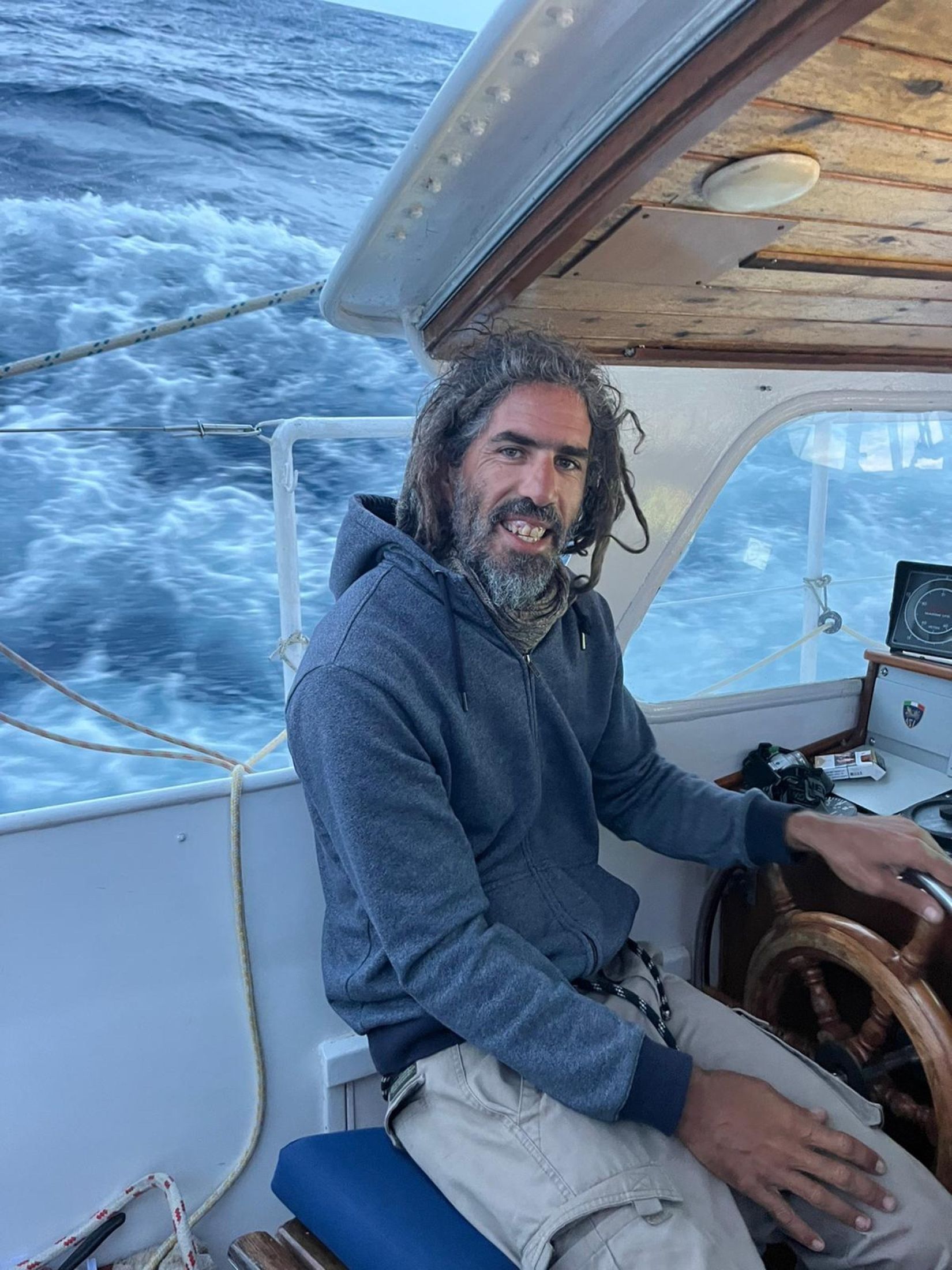 Franco at the wheel of a sailing yacht, smiling at the camera